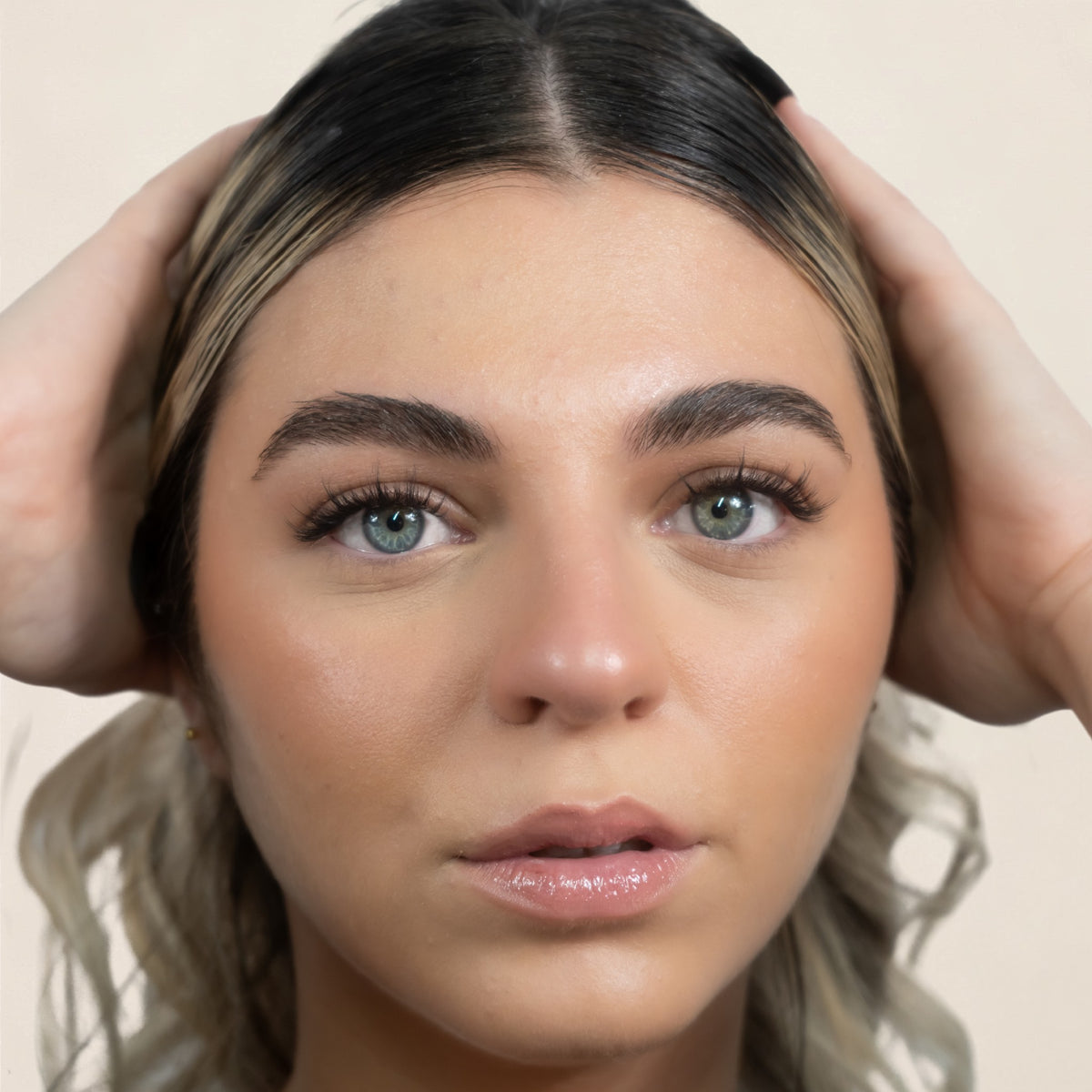 Femme aux yeux clairs de face, mains dans les cheveux, cils VOGUE posés