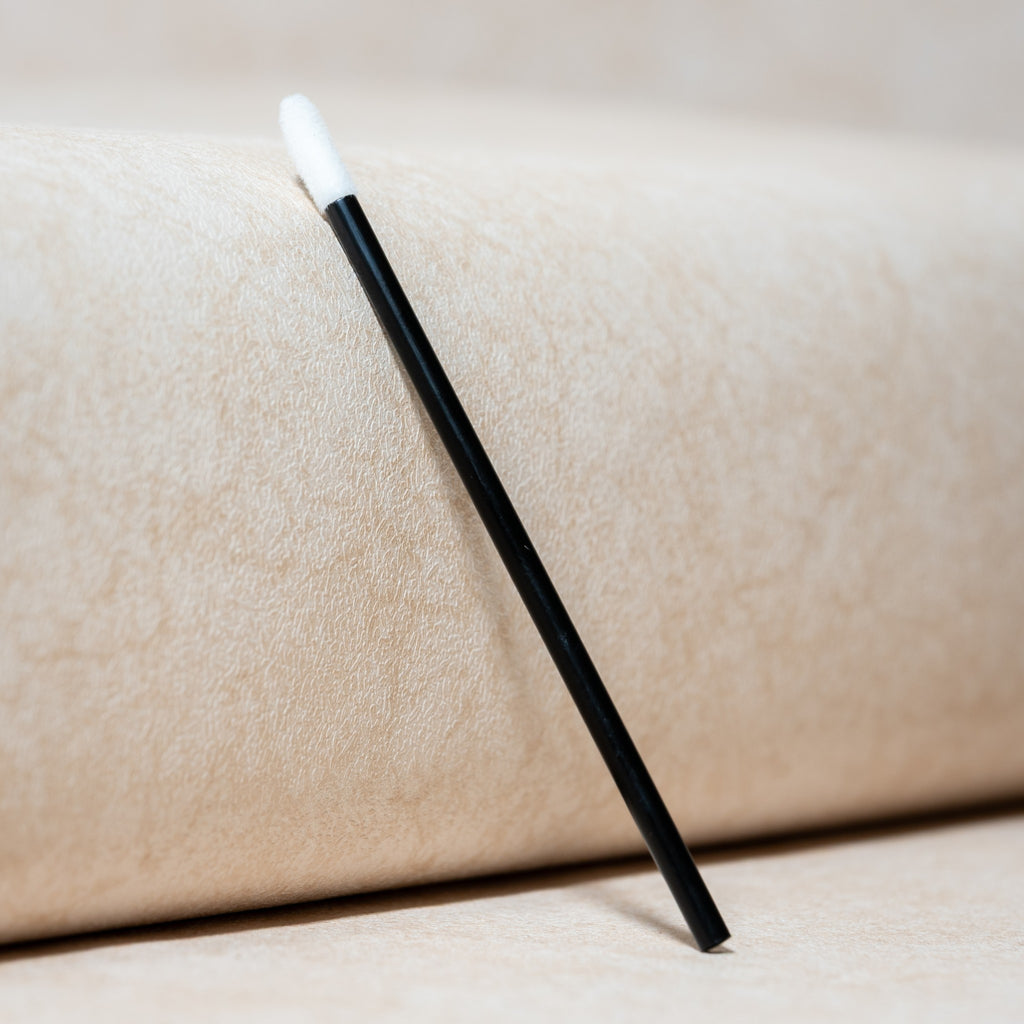 Bâtonnet nettoyant pour cils noir à embout blanc sur fond beige