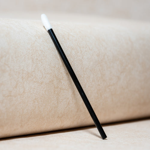 Bâtonnet nettoyant pour cils noir à embout blanc sur fond beige