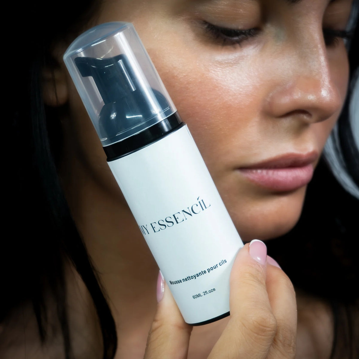 Femme tenant le flacon de mousse nettoyante pour cils contre sa joue