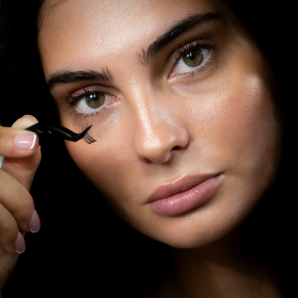 Femme brune appliquant ses faux cils avec la pince applicatrice noire