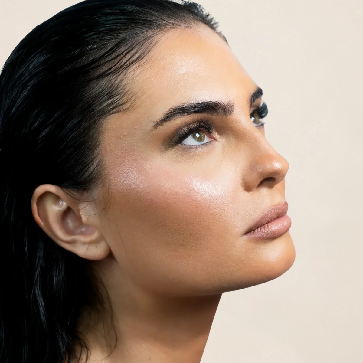 Profil d'une femme brune aux cheveux plaqués, regard vers le haut et faux cils
