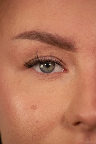Gros plan sur un œil gris-vert avec les faux cils press-on VOGUE