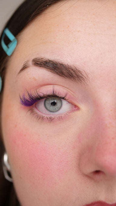 Gros plan sur un œil gris avec des faux cils press-on violets
