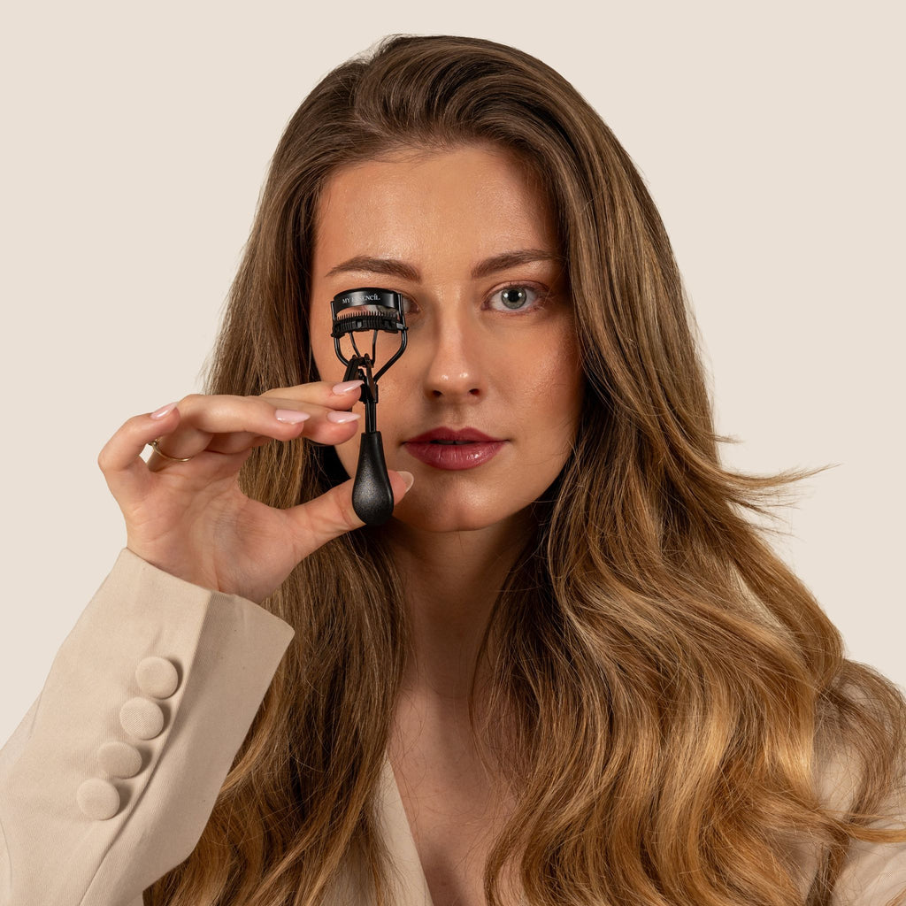 Femme aux cheveux longs tenant le recourbe-cils MyEssencìl devant son œil